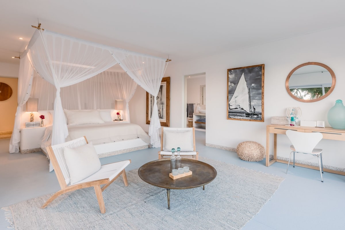 A bedroom with a canopy bed, a round coffee table, and a desk with a chair.