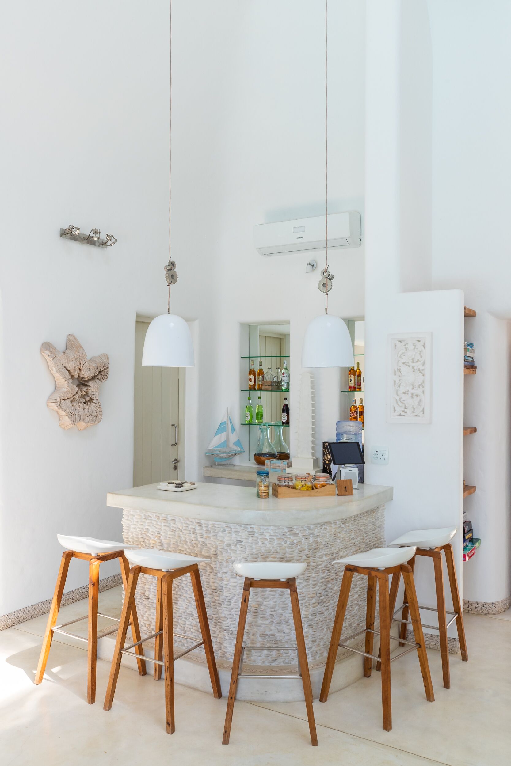 A modern kitchen with a central island, wooden bar stools, pendant lights, and a view into the adjacent dining area.