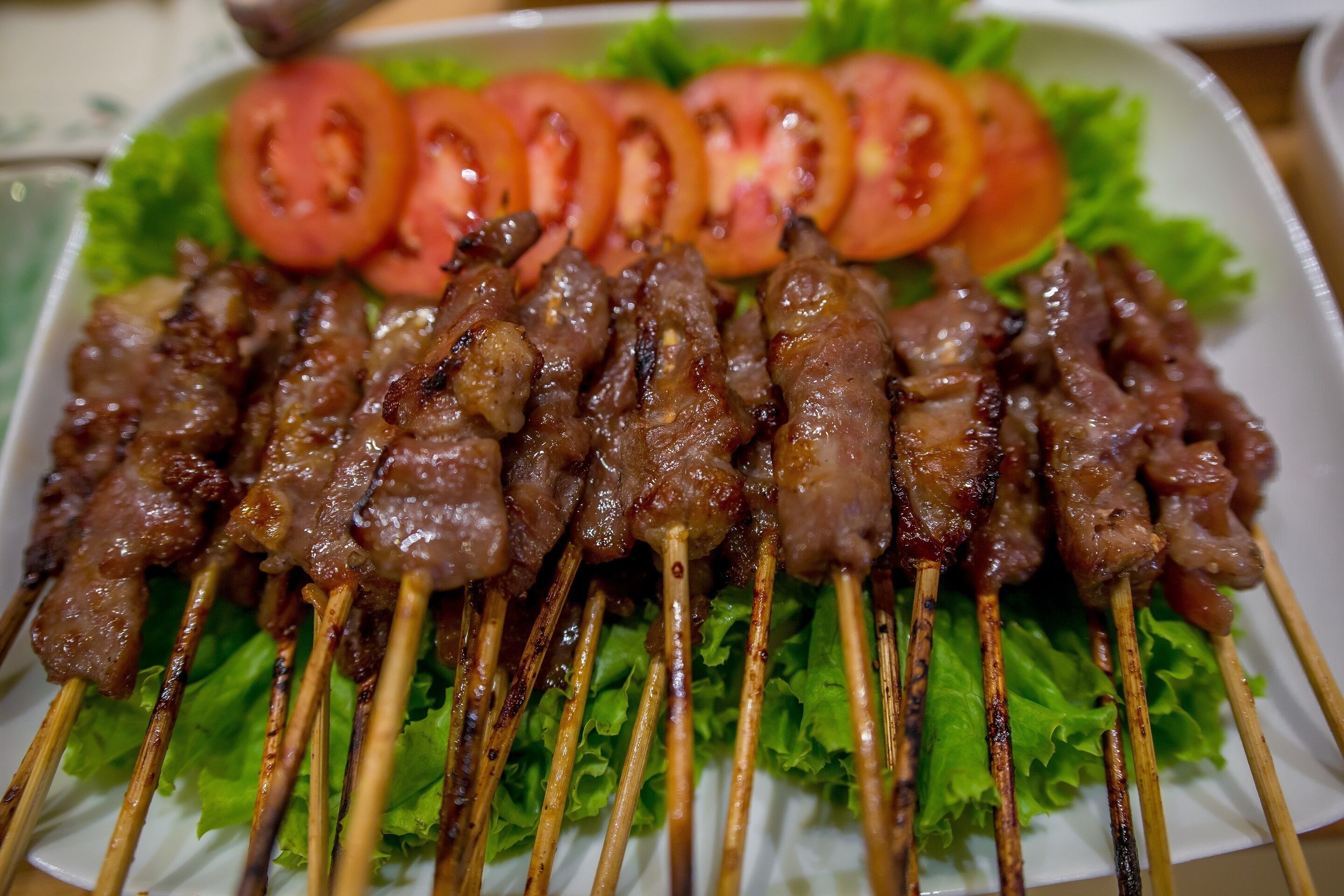 A plate of grilled meat skewers with lettuce and sliced tomatoes.