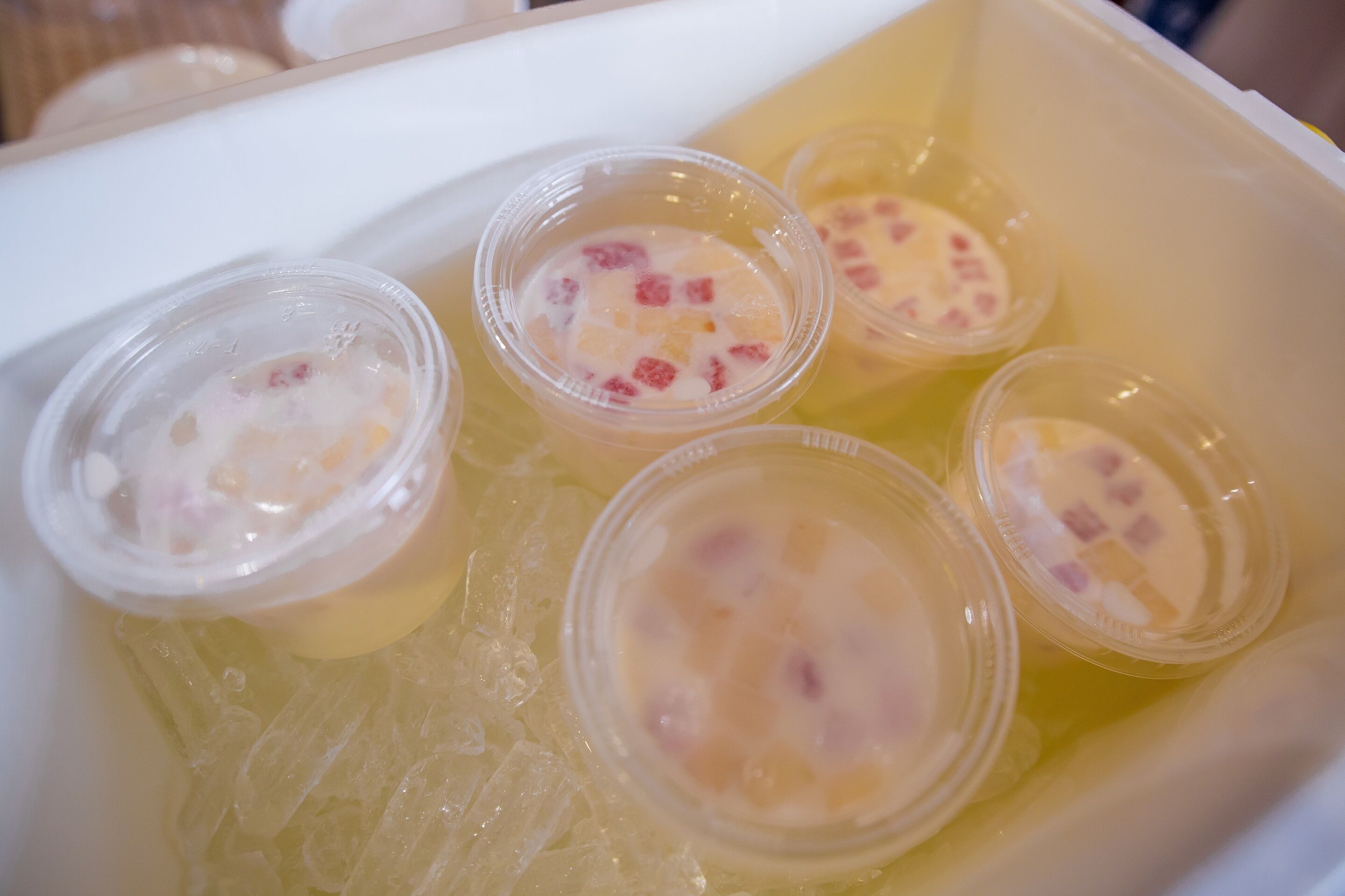 A container with several plastic cups filled with a yellow liquid and small red pieces.