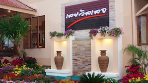 A hotel lobby with a large sign, two large vases, and colorful flower arrangements. - Loei Village Hotel (Mueang Loei)