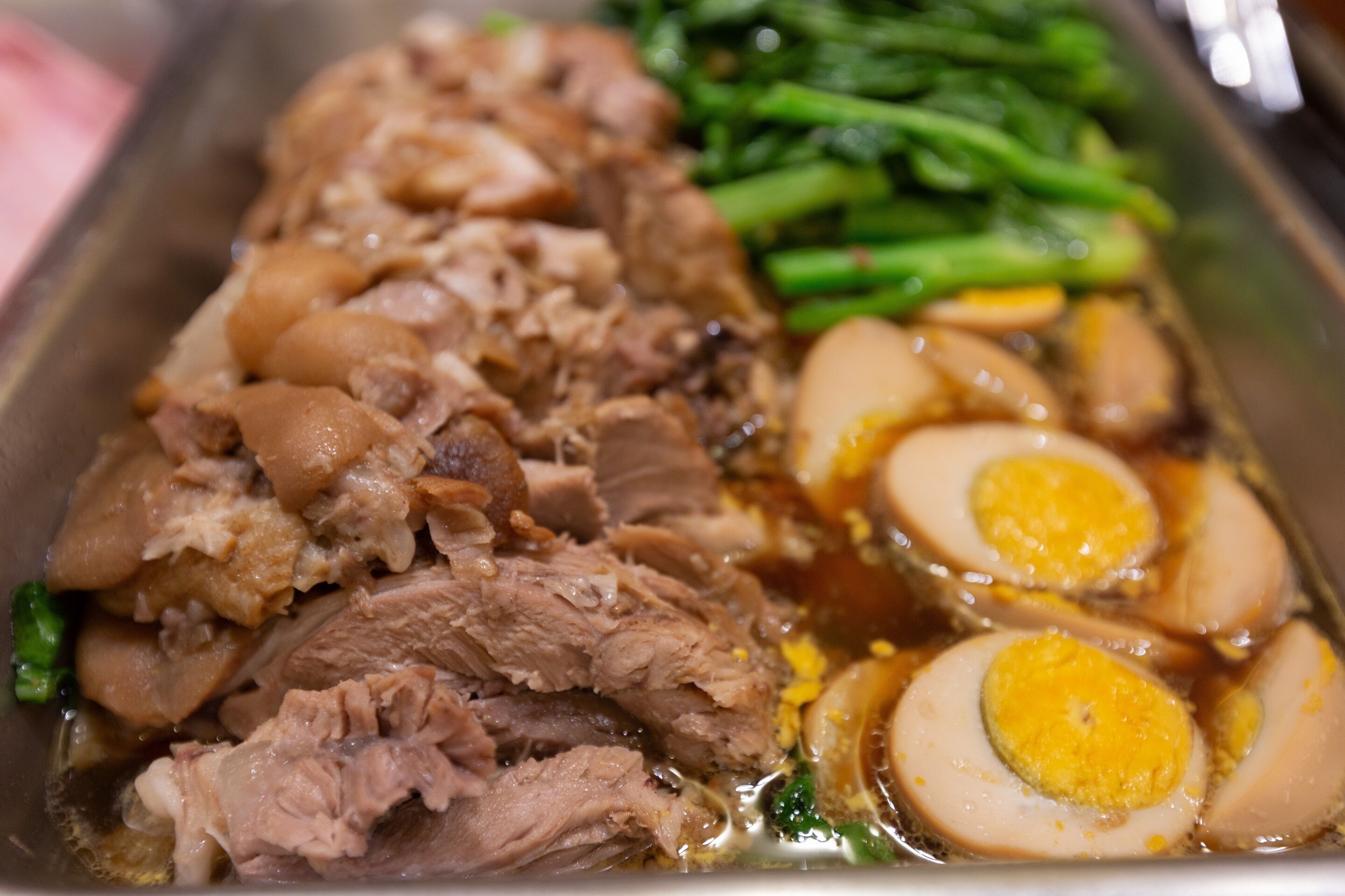 A dish with sliced meat and boiled eggs in a broth.