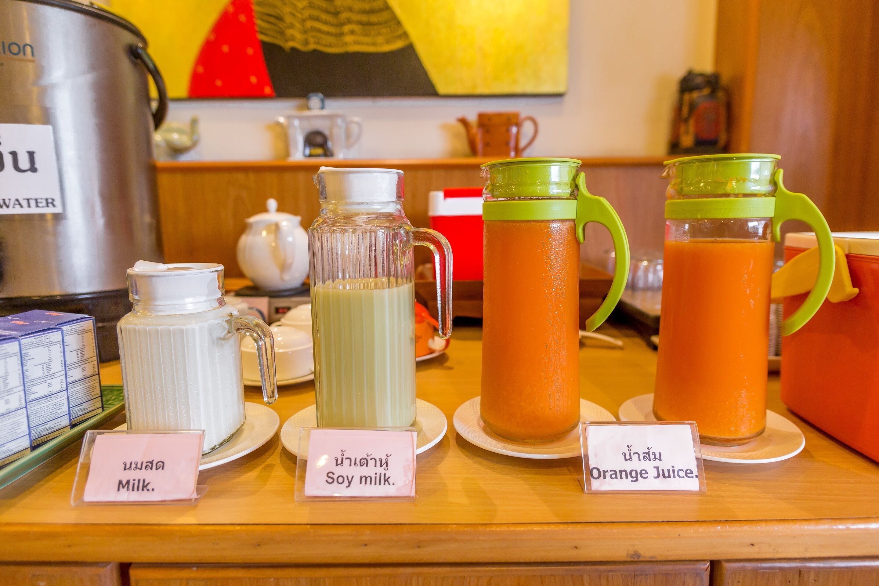 A beverage station with labeled containers of milk, soy milk, and orange juice.