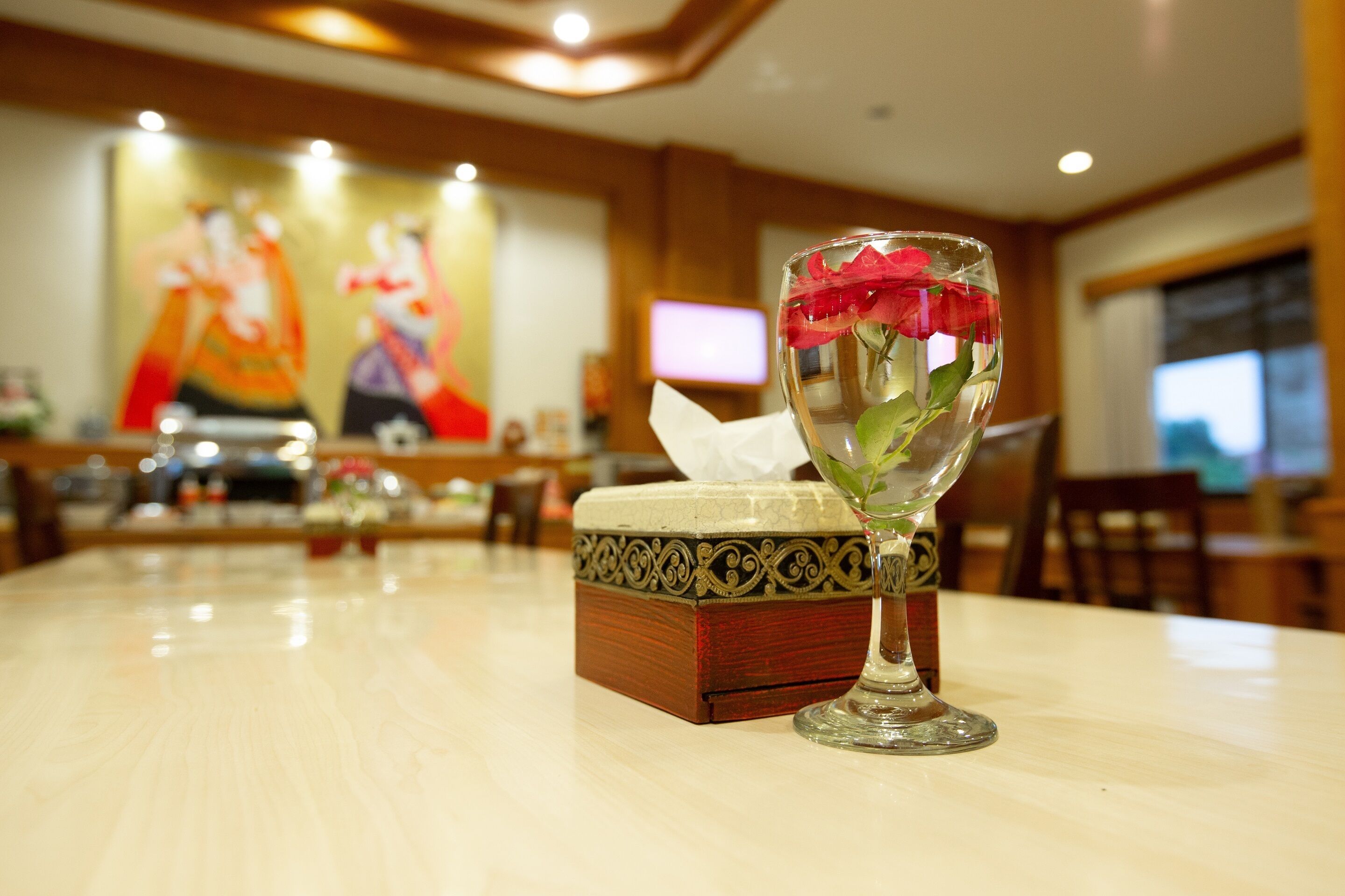 A table with a glass containing a flower and a decorative box.