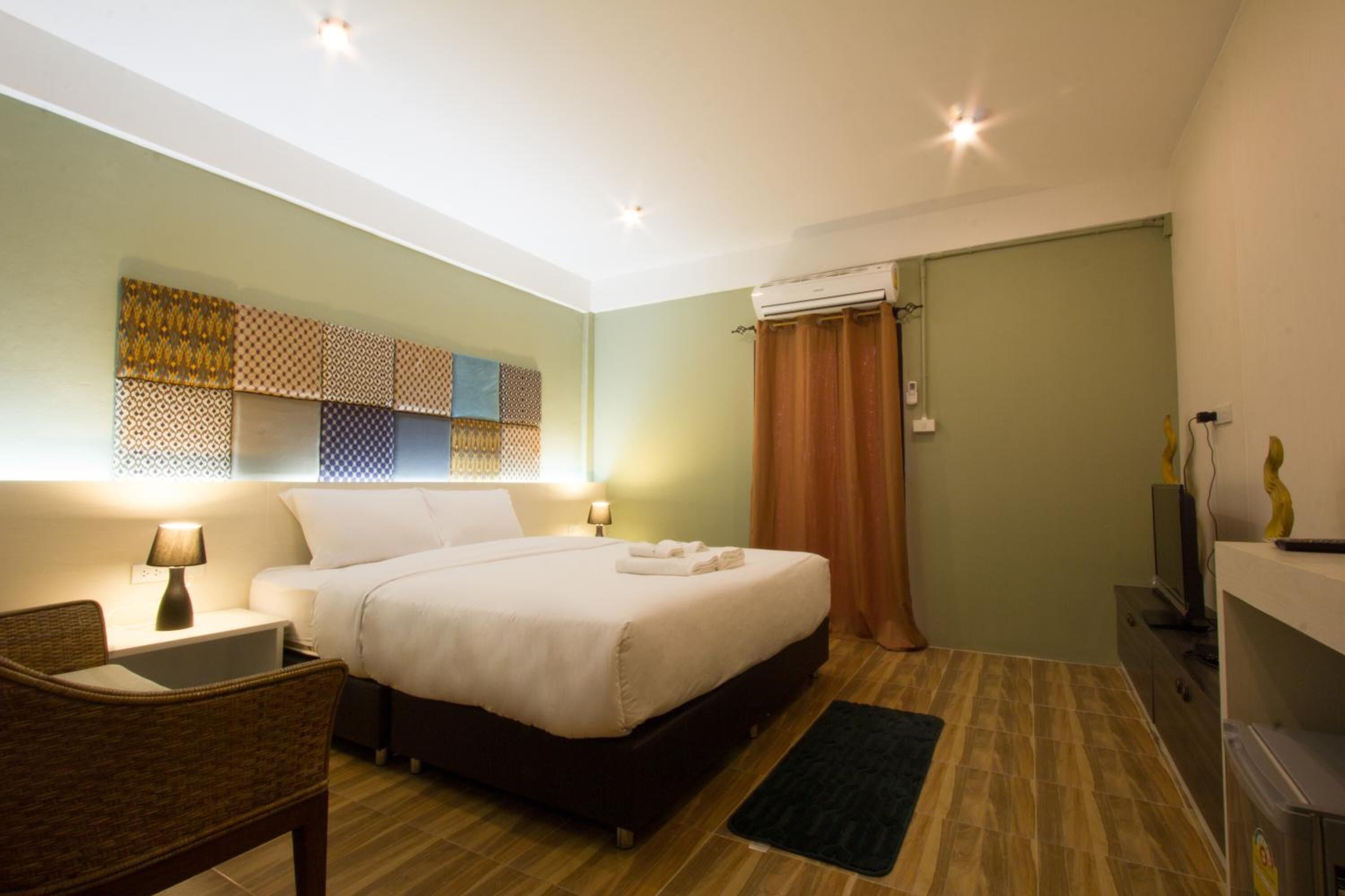 A hotel room with a bed, bedside lamps, a flat-screen TV, a wall-mounted air conditioner, and a patterned wall decoration.