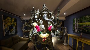 A statue of a deity in a room with a sofa, a table, and a painting on the wall. - At Ease Bijou Place (Chiang Mai)