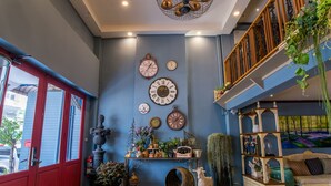 A room with a blue wall, a red door, and a ceiling with a decorative light fixture. There are clocks on the wall and a shelf with various items. - At Ease Bijou Place (Chiang Mai)