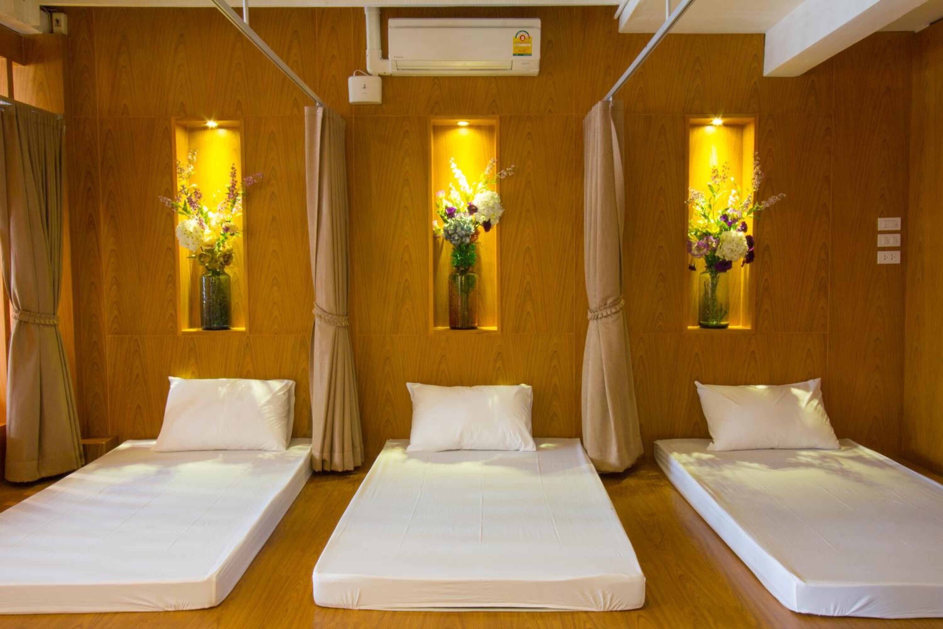 A hotel room with three single beds, wooden walls, and floral decorations in the windows.