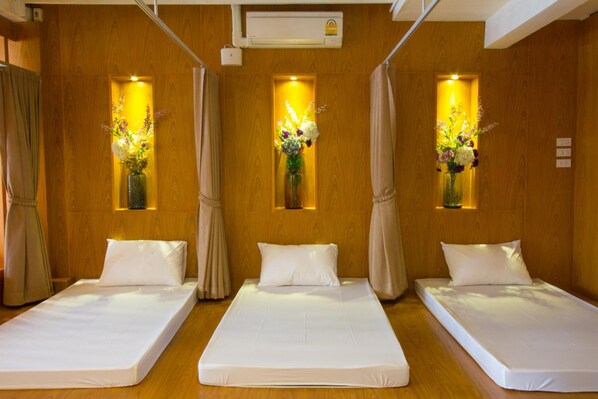 A hotel room with three single beds, wooden walls, and floral decorations in the windows. - At Ease Bijou Place (Chiang Mai)