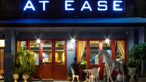 A hotel entrance with a neon sign, red doors, and outdoor seating with a horse sculpture. - At Ease Bijou Place (Chiang Mai)