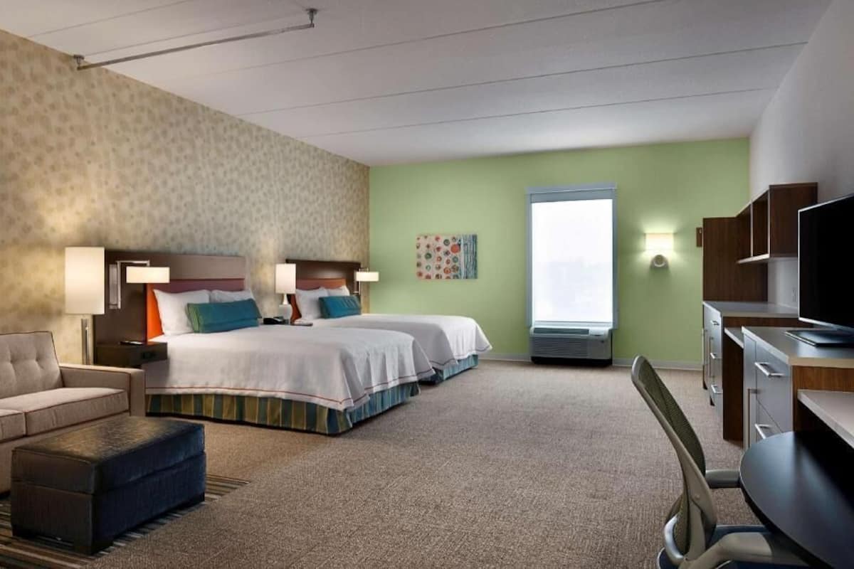 A hotel room with two beds, a sofa, a desk, and a TV.