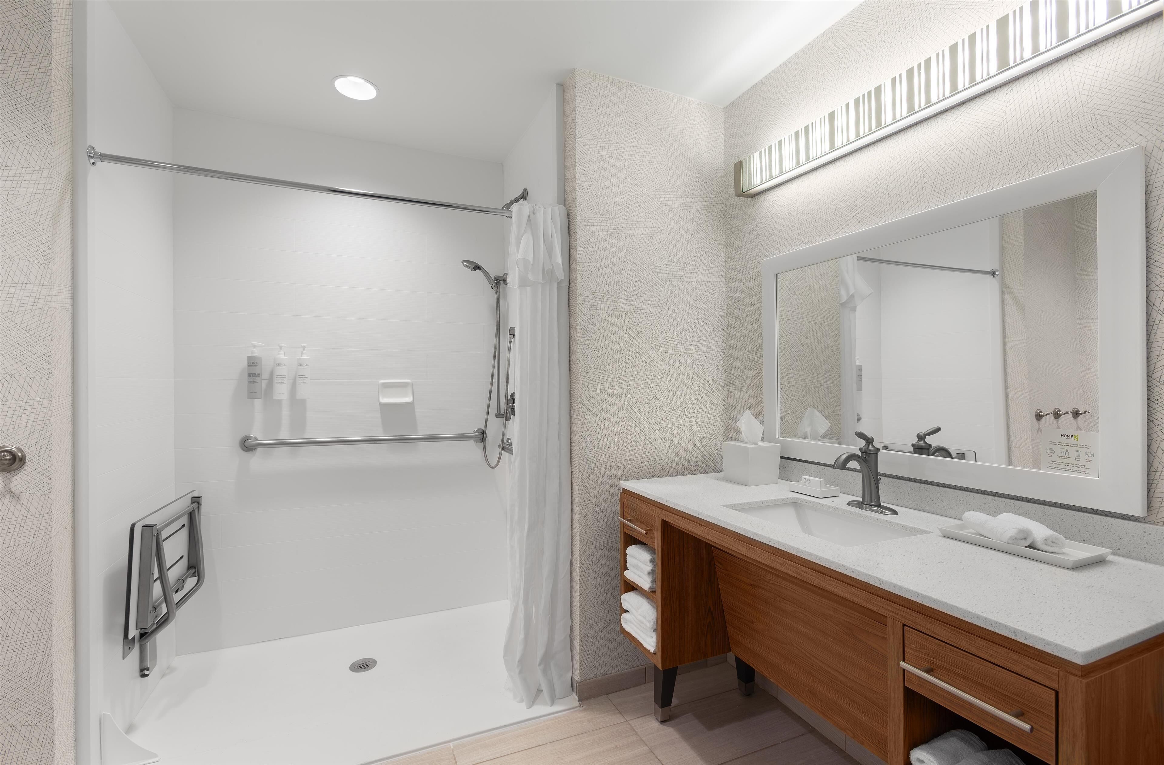 Un baño moderno con cabina de ducha, tocador de madera con un espejo grande y lavabo blanco.