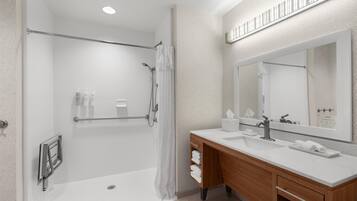 Un baño moderno con cabina de ducha, tocador de madera con un espejo grande y lavabo blanco.
