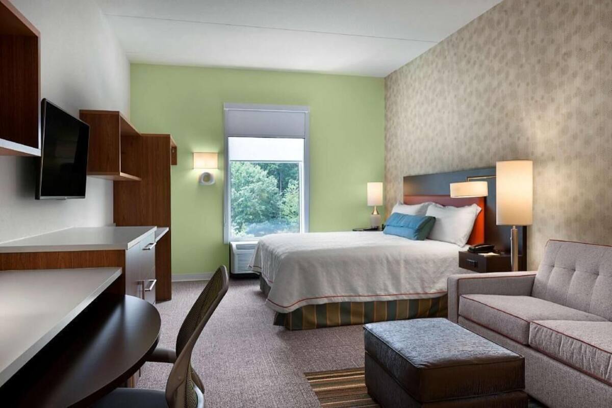 A hotel room with a bed, desk, chair, and a television.