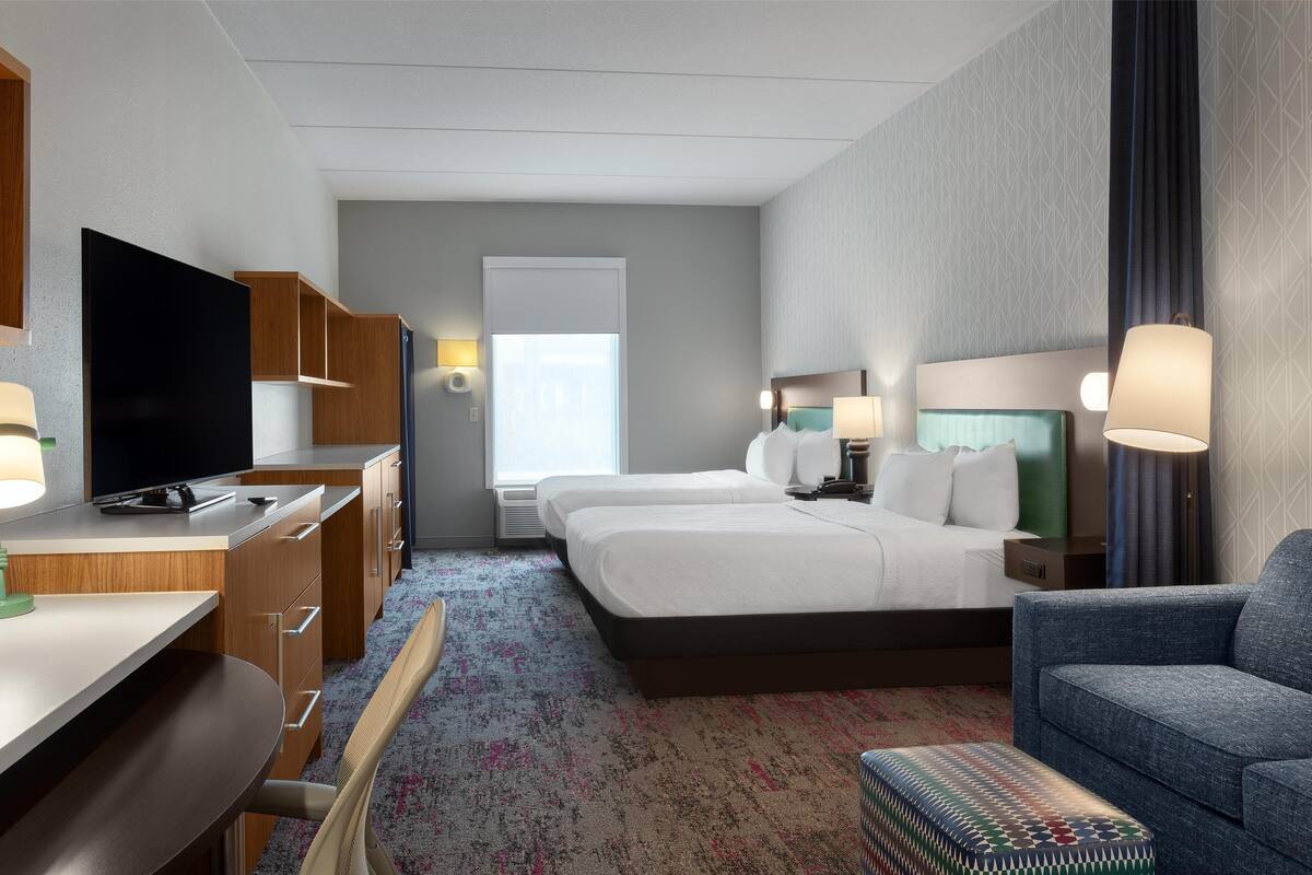 A hotel room with a bed, a desk, a TV, and a chair.