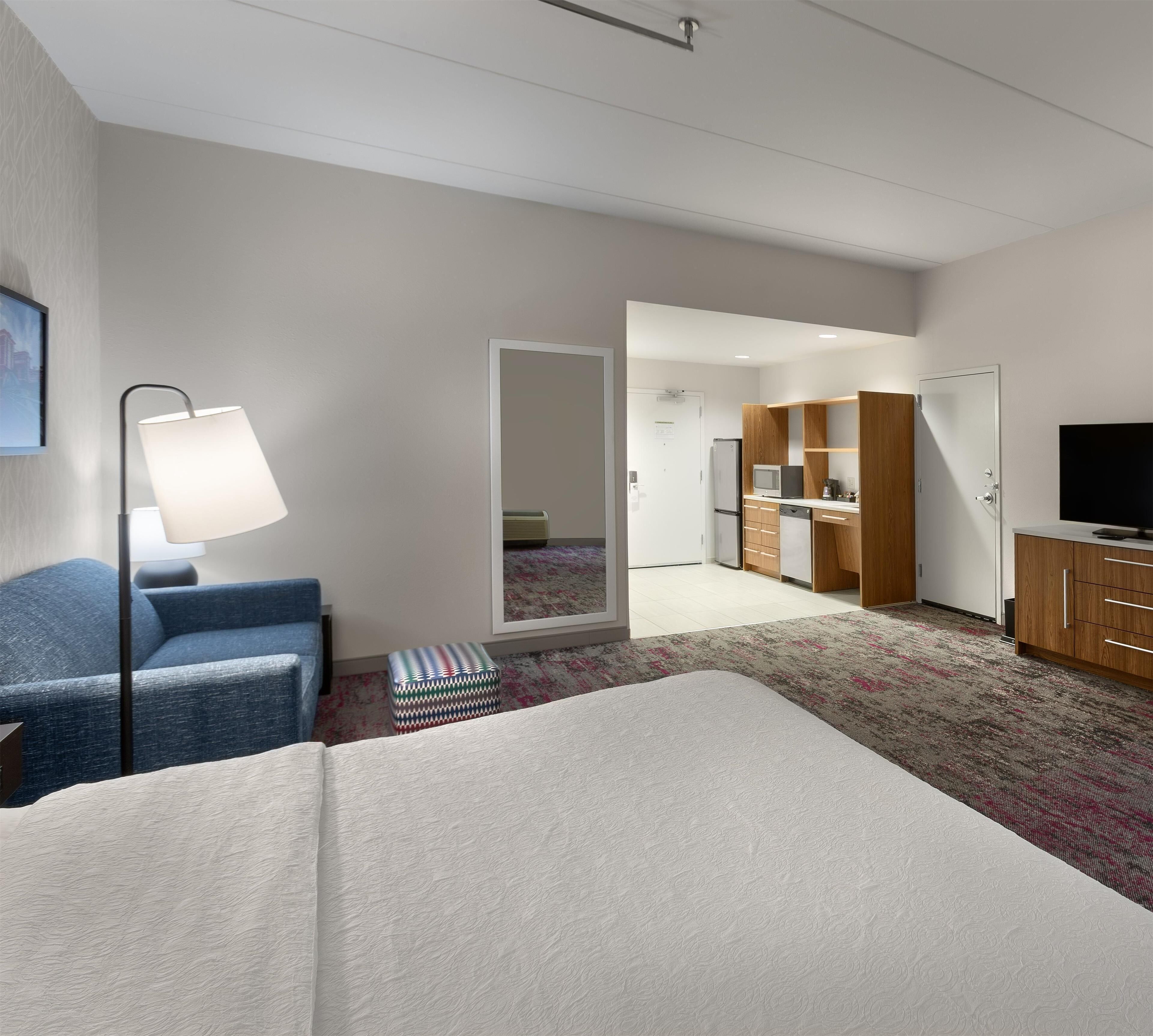 Hotellihuone, jossa on sänky, työpöytä, tuoli, lamppu, televisio ja pieni keittiönurkkaus.