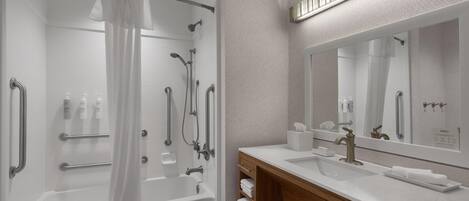 A modern bathroom with a walk-in shower, grab bars, a large mirror, and a wooden vanity with a sink.