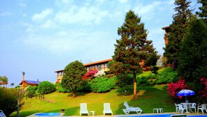 A swimming pool with lounge chairs and a view of a hillside with trees and a building. - Hotel Bangalôs da Serra (Gramado)