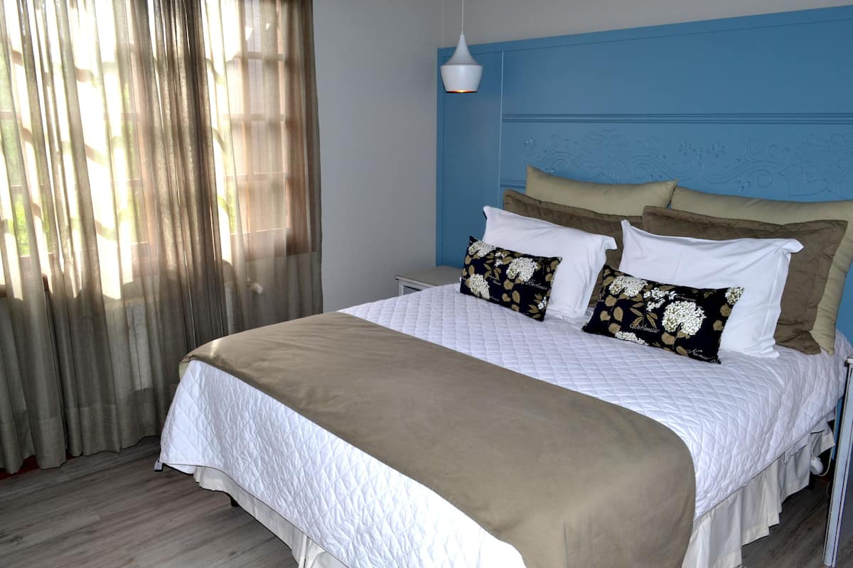 Una cama bien tendida con colcha blanca y beige, un cabecero azul y varias almohadas.