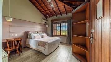 A bedroom with a wooden ceiling, a bed with floral bedding, a wooden chair, and a window with a view.