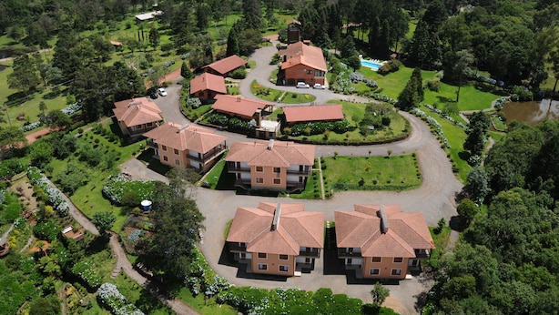 An aerial view of a residential complex with multiple houses, a central building, and surrounding greenery. - Hotel Bangalôs da Serra (Gramado)