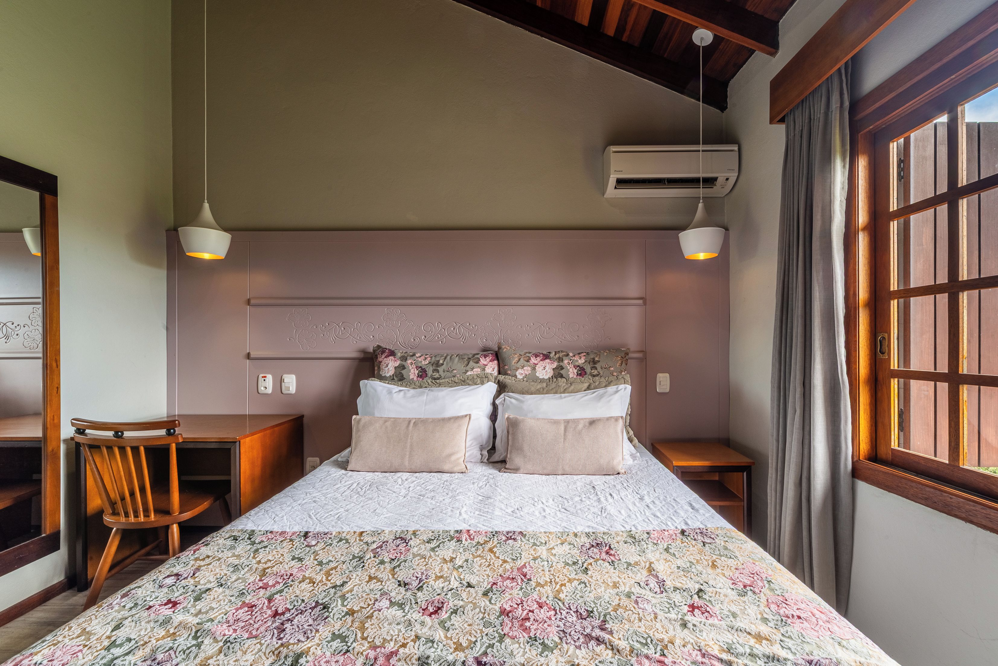 Un dormitorio con cama, dos mesitas de noche, una silla, un equipo de aire acondicionado y una ventana con cortinas.