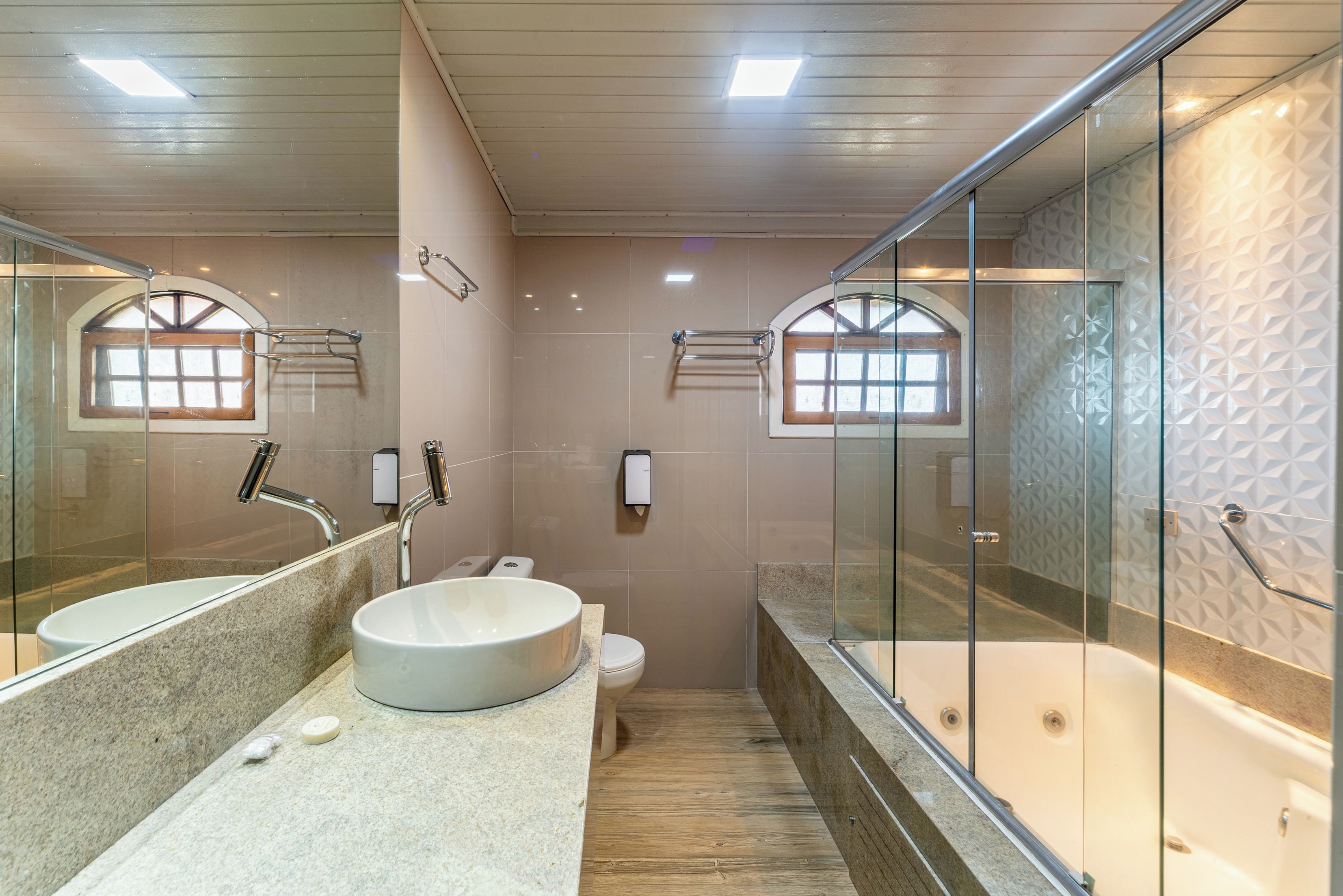 A modern bathroom with a large mirror, a round sink, a toilet, and a bathtub.