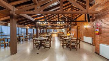 A spacious restaurant with high ceilings, exposed wooden beams, and brick walls. Tables and chairs are arranged for dining.