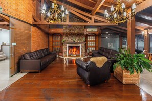A spacious living area with a fireplace, leather sofas, and a large plant. - Hotel Bangalôs da Serra (Gramado)