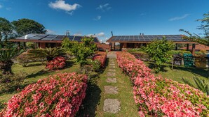 A building with solar panels on the roof, surrounded by well-maintained gardens and a stone pathway. - Hotel Bangalôs da Serra (Gramado)