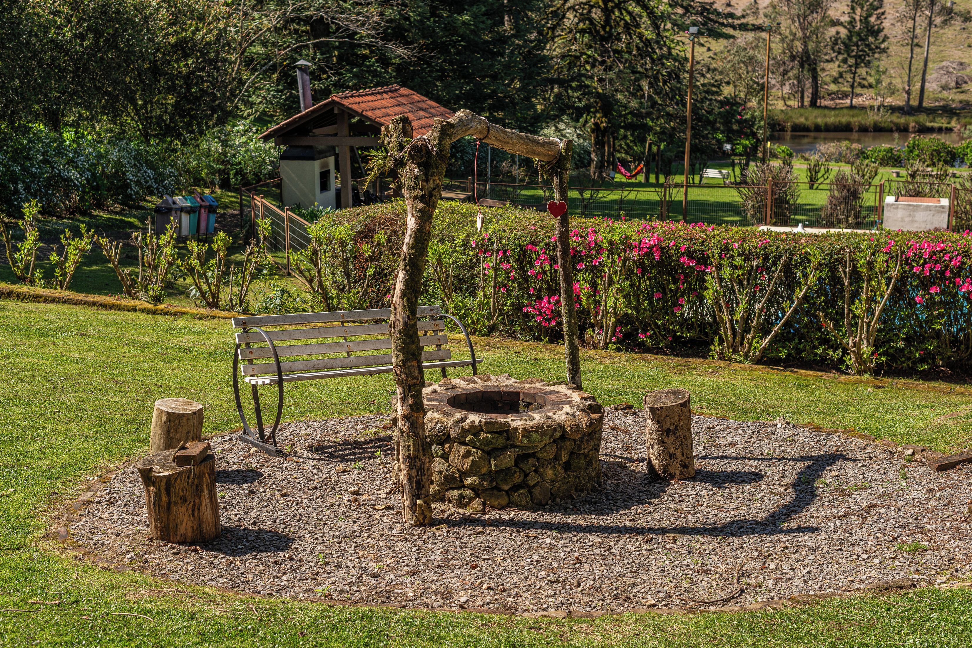 A rustic outdoor seating area with a stone fire pit, wooden benches, and a small wooden structure.