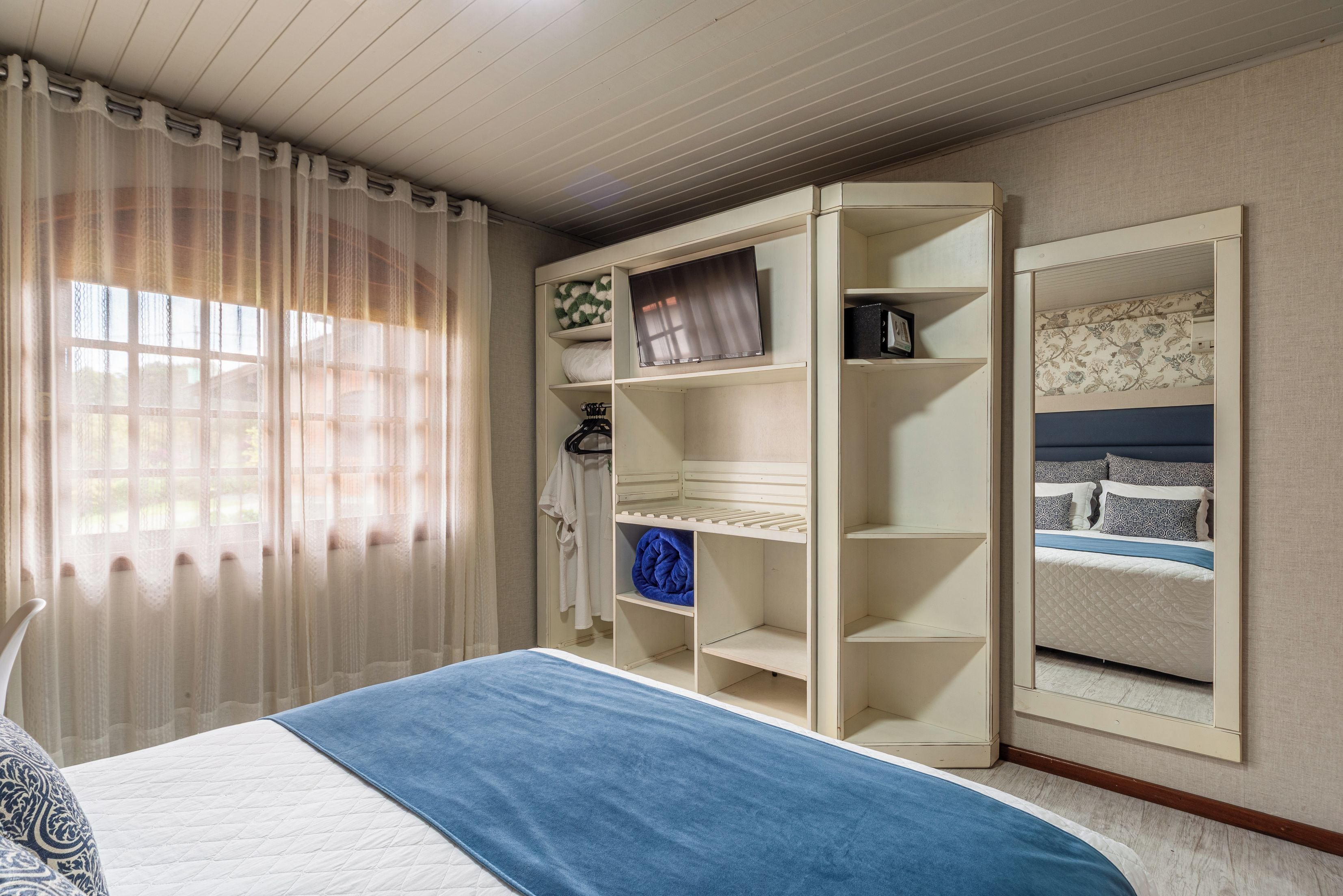 Quarto com cama, guarda-roupa e televisão integrada.