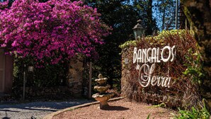 A garden with a stone fountain, a pink flowering bush, and a sign reading 'BANGALOS Garden'. - Hotel Bangalôs da Serra (Gramado)