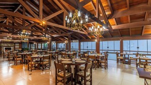 A spacious dining area with high wooden beams, multiple chandeliers, and large windows offering a view. - Hotel Bangalôs da Serra (Gramado)