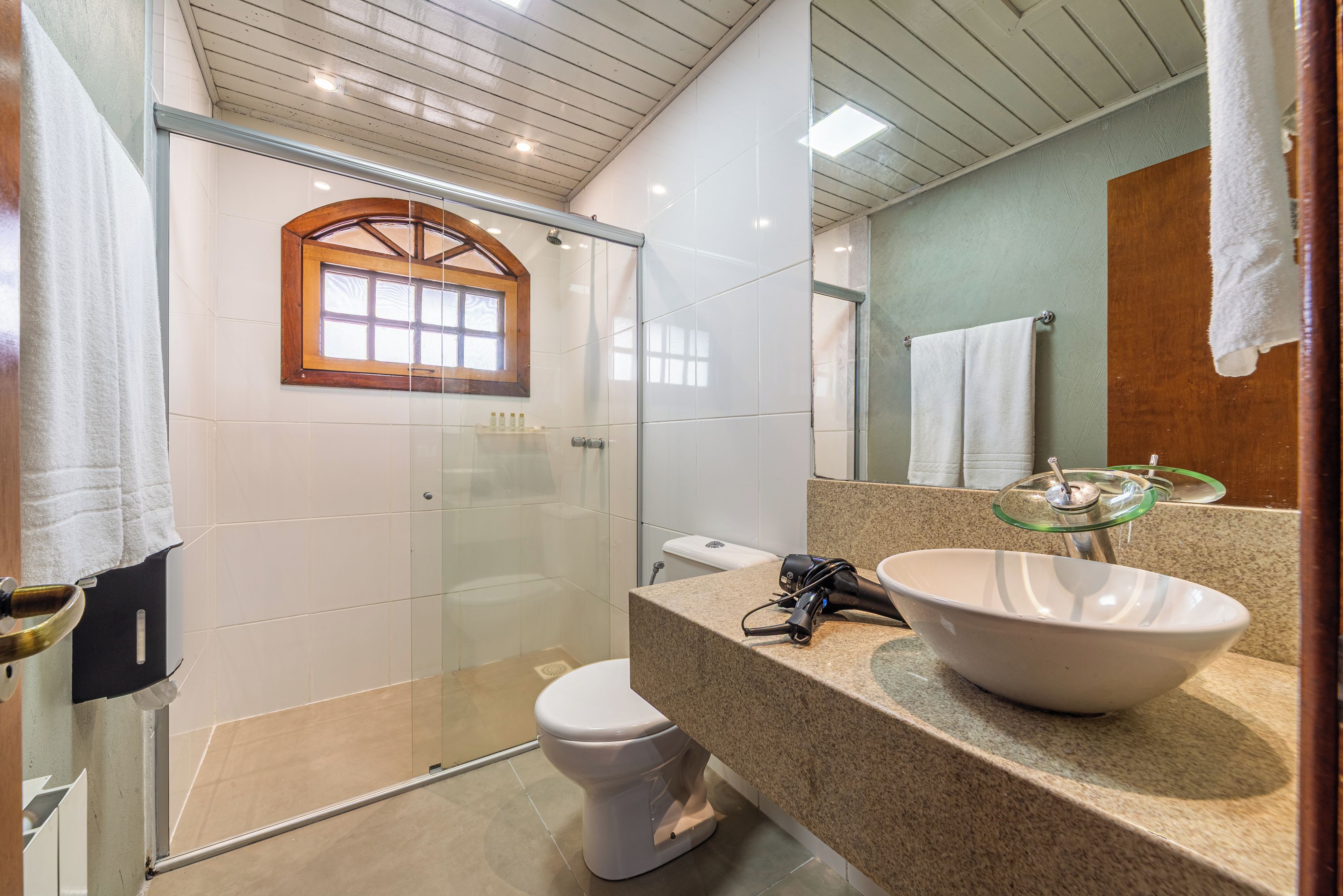 A bathroom with a glass shower enclosure, a white toilet, a sink with a large basin, and a mirror with a wooden frame.