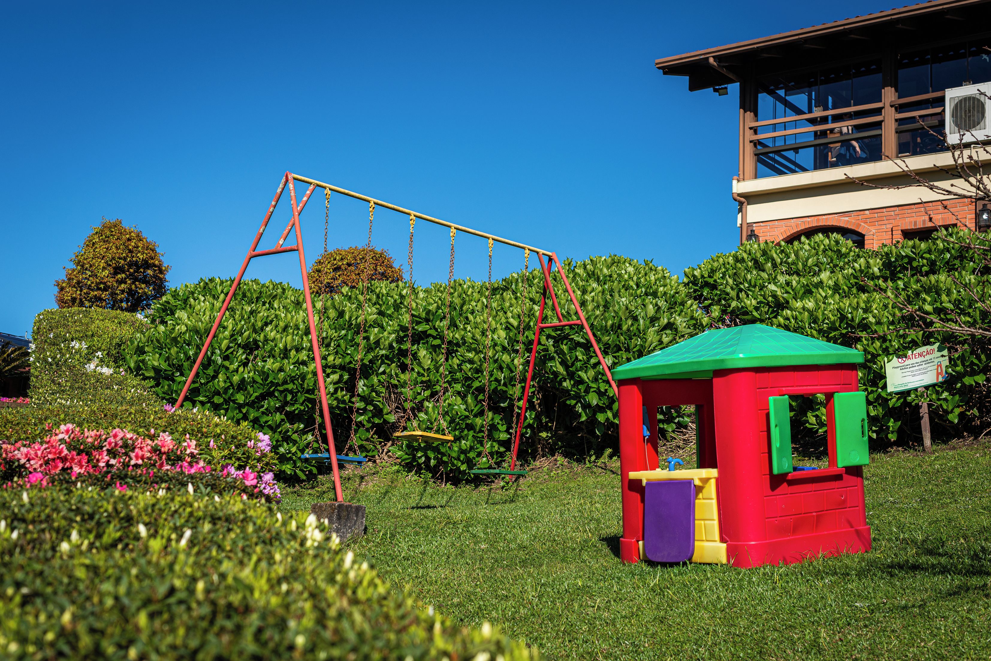 Um parquinho com balanços e uma casinha de brinquedo vermelha.