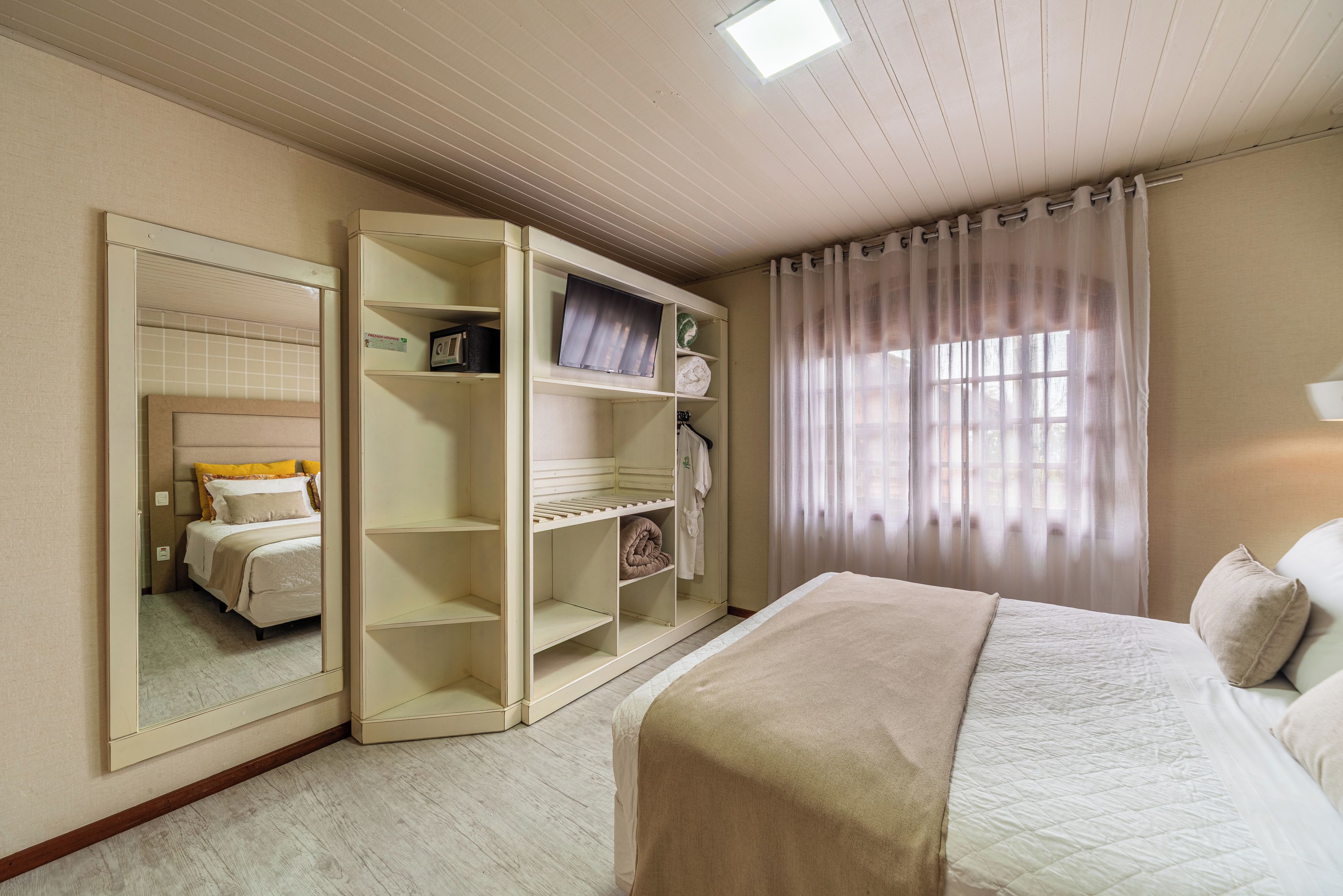 Ein Schlafzimmer mit einem Bett, einem Kleiderschrank, einem Spiegel und einem Fenster mit Vorhängen.
