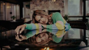 A person leaning on a reflective surface in a room with a fireplace and a window. - Hotel Bangalôs da Serra (Gramado)
