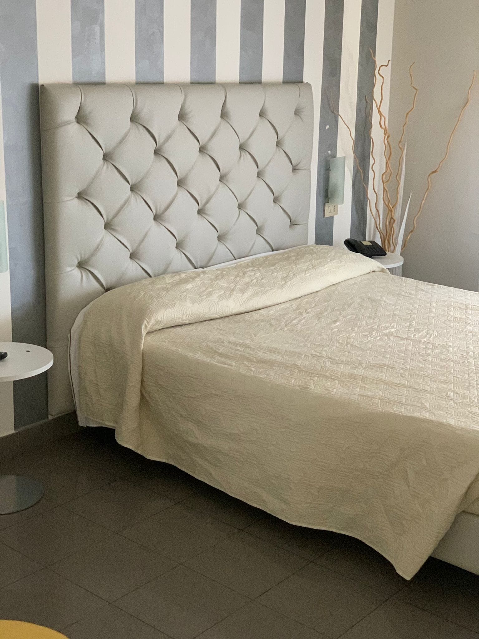 Una camera da letto con una testiera trapuntata, un letto con copriletto texturizzato, un comodino e una parete a righe verticali.