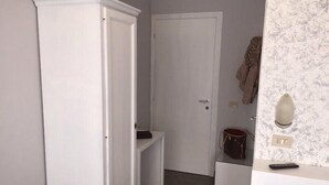 A room with a white wardrobe, a door, a small shelf, a mirror, and a remote control on a counter. - Hotel Marte (Milan)