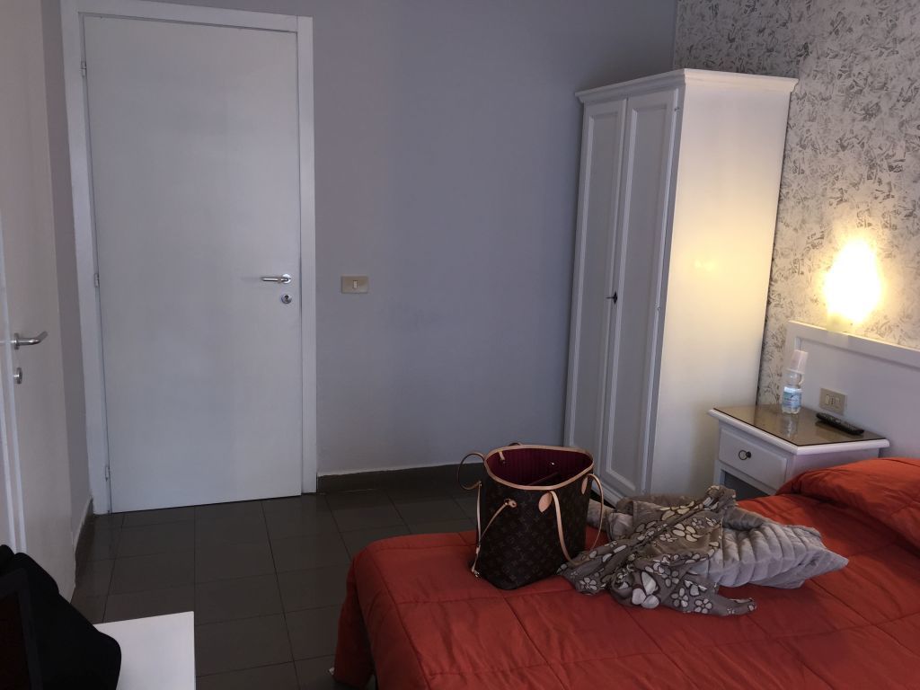 Une chambre d’hôtel avec un lit, une armoire, une table de chevet avec une lampe et une porte.