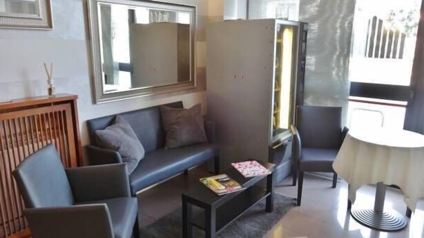 A modern living room with a grey sofa, a coffee table with magazines, a small round table, and a large mirror on the wall. - Hotel Marte (Milan)