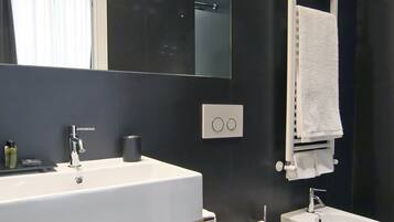 Een moderne badkamer met een wit wastafel, twee toiletten, een spiegel en een handdoekrek.