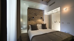 Une chambre moderne avec un mur d’accent en briques, un grand lit recouvert d’une couette marron, deux lampes de chevet et un grand miroir sur toute la longueur du mur.