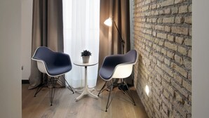 Une pièce avec un mur en briques, deux chaises modernes, une petite table et une fenêtre avec des rideaux.