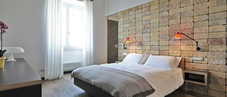 A modern bedroom with a large bed, a wooden nightstand, a potted plant, and a brick-patterned wall.