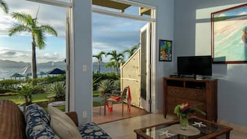A living room with a view of the ocean, a television, and a wooden cabinet.