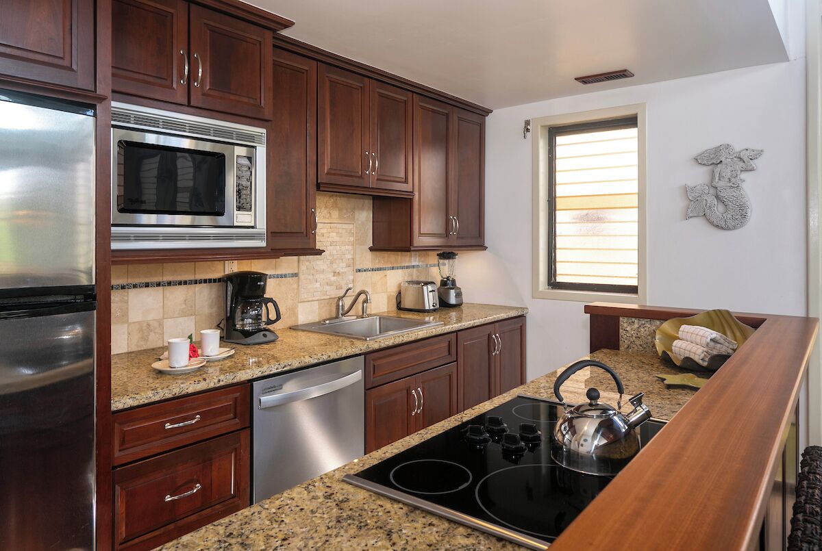 A kitchen with dark wooden cabinets, a stainless steel refrigerator, a microwave, a coffee maker, a kettle, and a dishwasher.