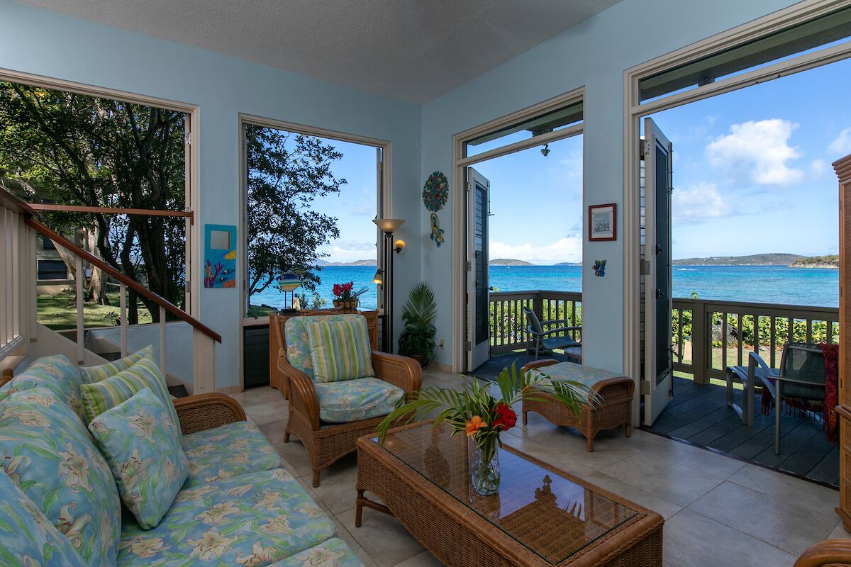 A spacious living room with a large window overlooking the sea, furnished with wicker sofas and a coffee table.