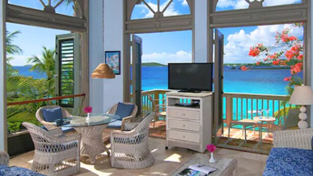 A room with a TV, wicker furniture, and a view of the ocean. - Suite St. John at Gallows Point Resort (St. John)